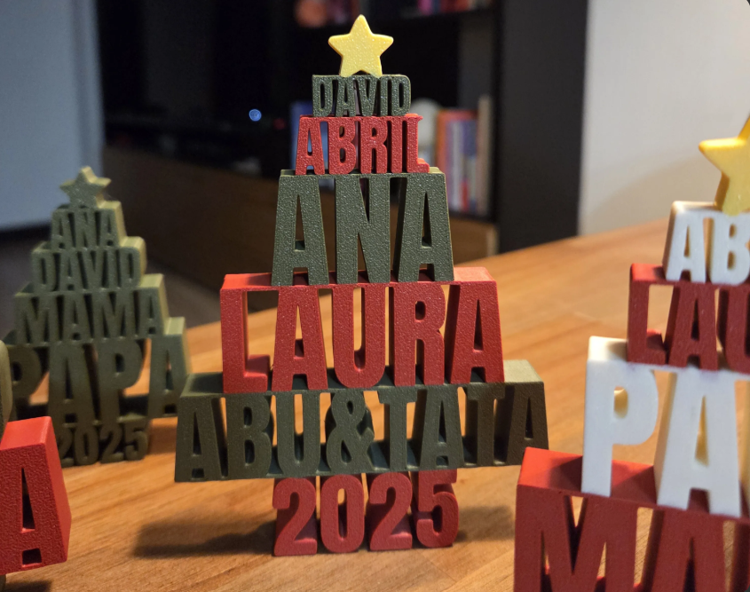 Personalized 3D-printed Christmas tree-shaped name signs displayed on a wooden table in a home setting.